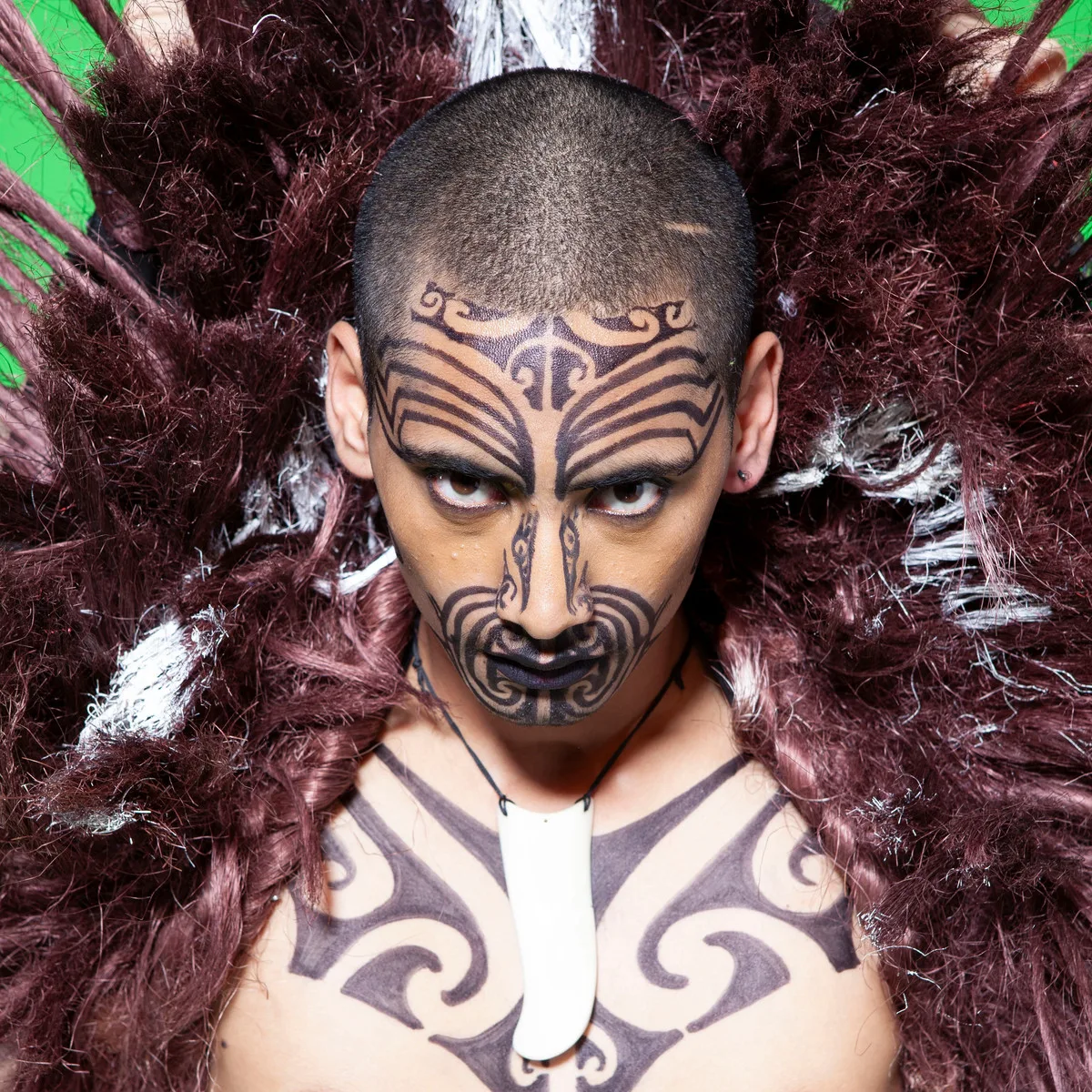 Māori performance artist wearing a feathered costume and moko-inspired stage makeup