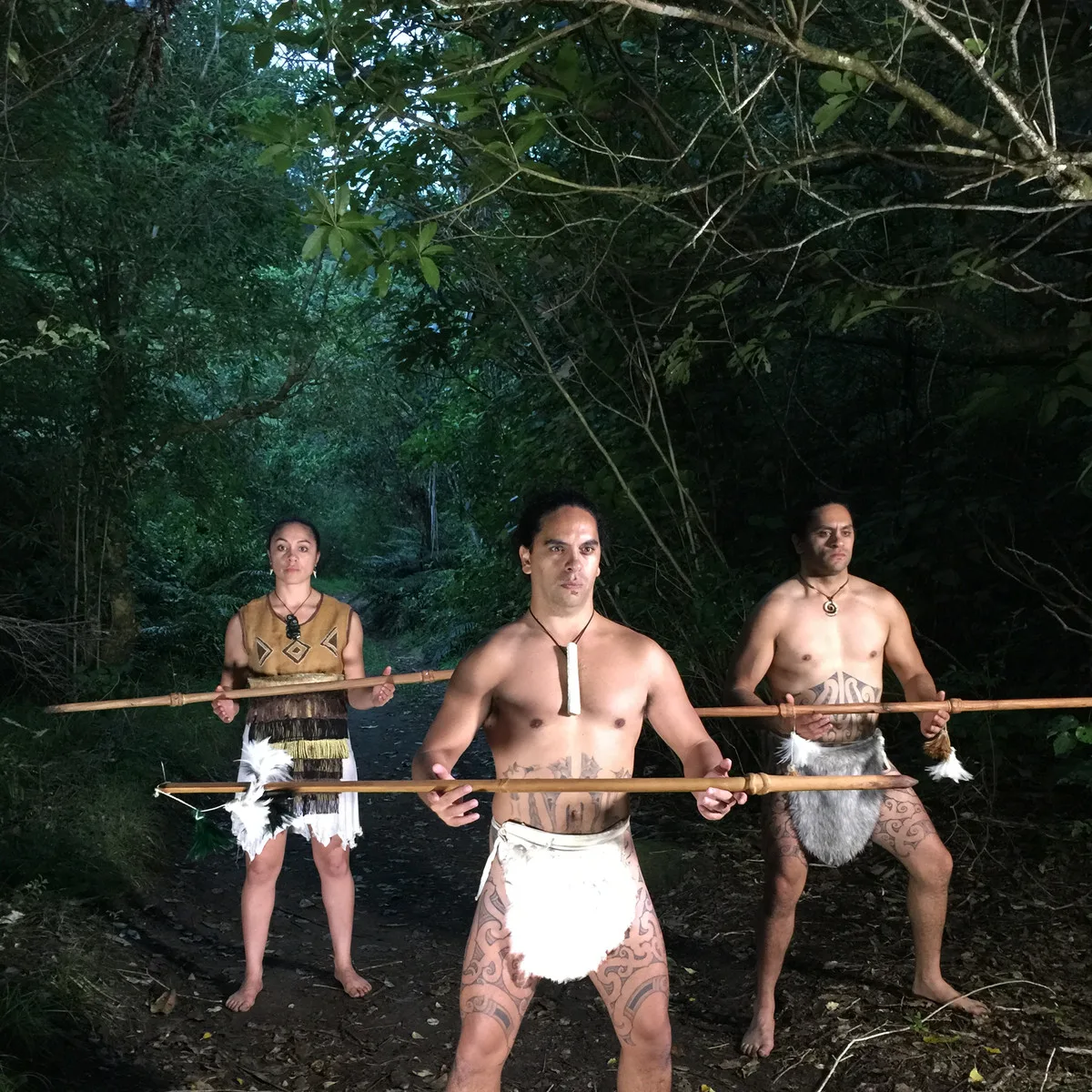 Three Māori performers in traditional dress standing in native bush